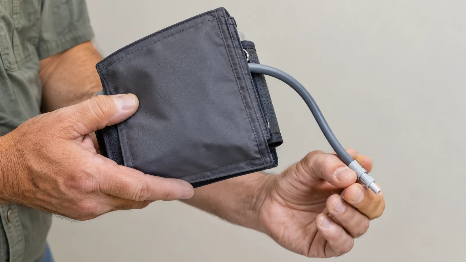 A person wrapping a large easy-wrap cuff around their own upper arm with one hand, monitor on the table